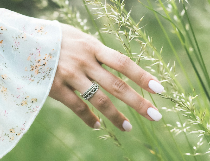 Hand with white-painted nails and a silver ring brushing through tall grass.