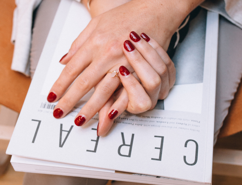 Hands with glossy red nails resting on a magazine.
