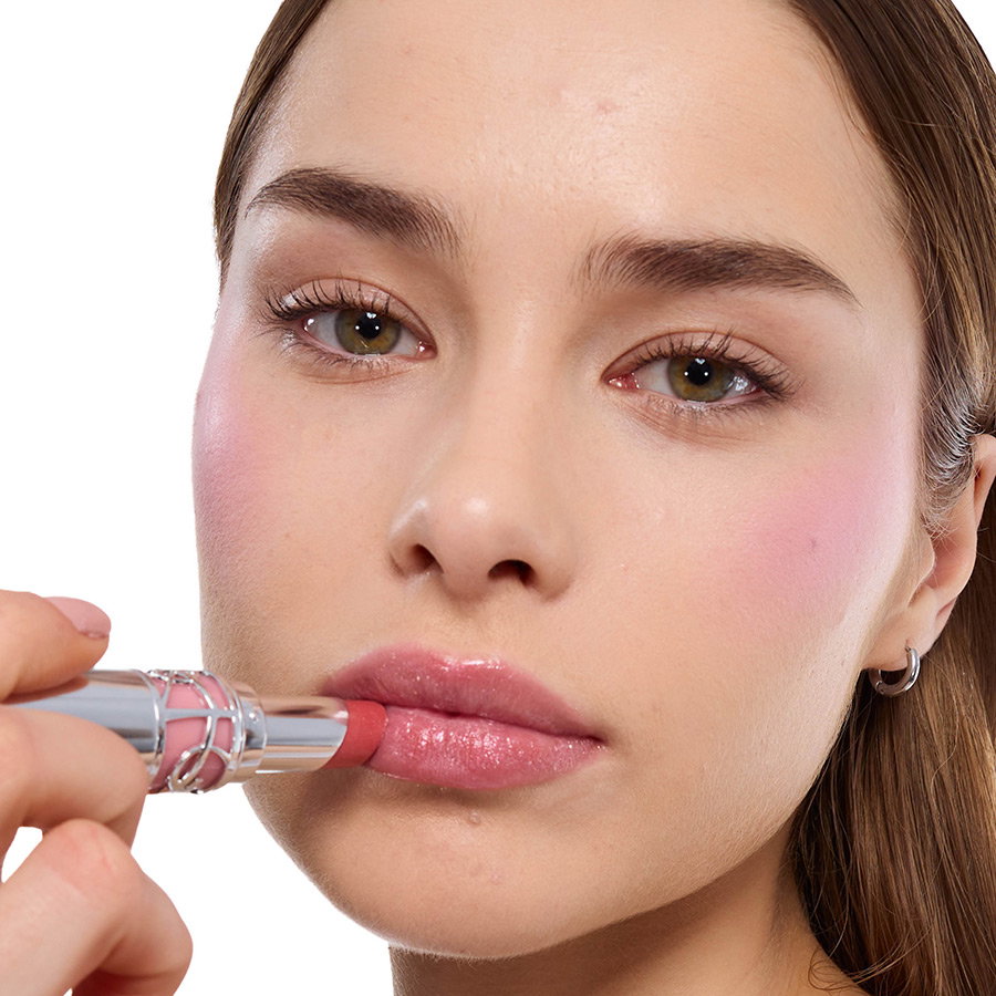 Close-up of a woman with light skin applying a shiny pink YSL lipstick to her lips.