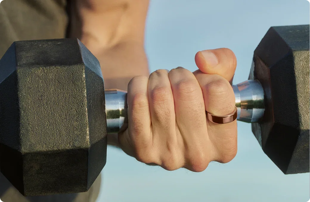 Close-up of a hand wearing a deep rose Oura Ring 5 gripping a dumbbell during a workout