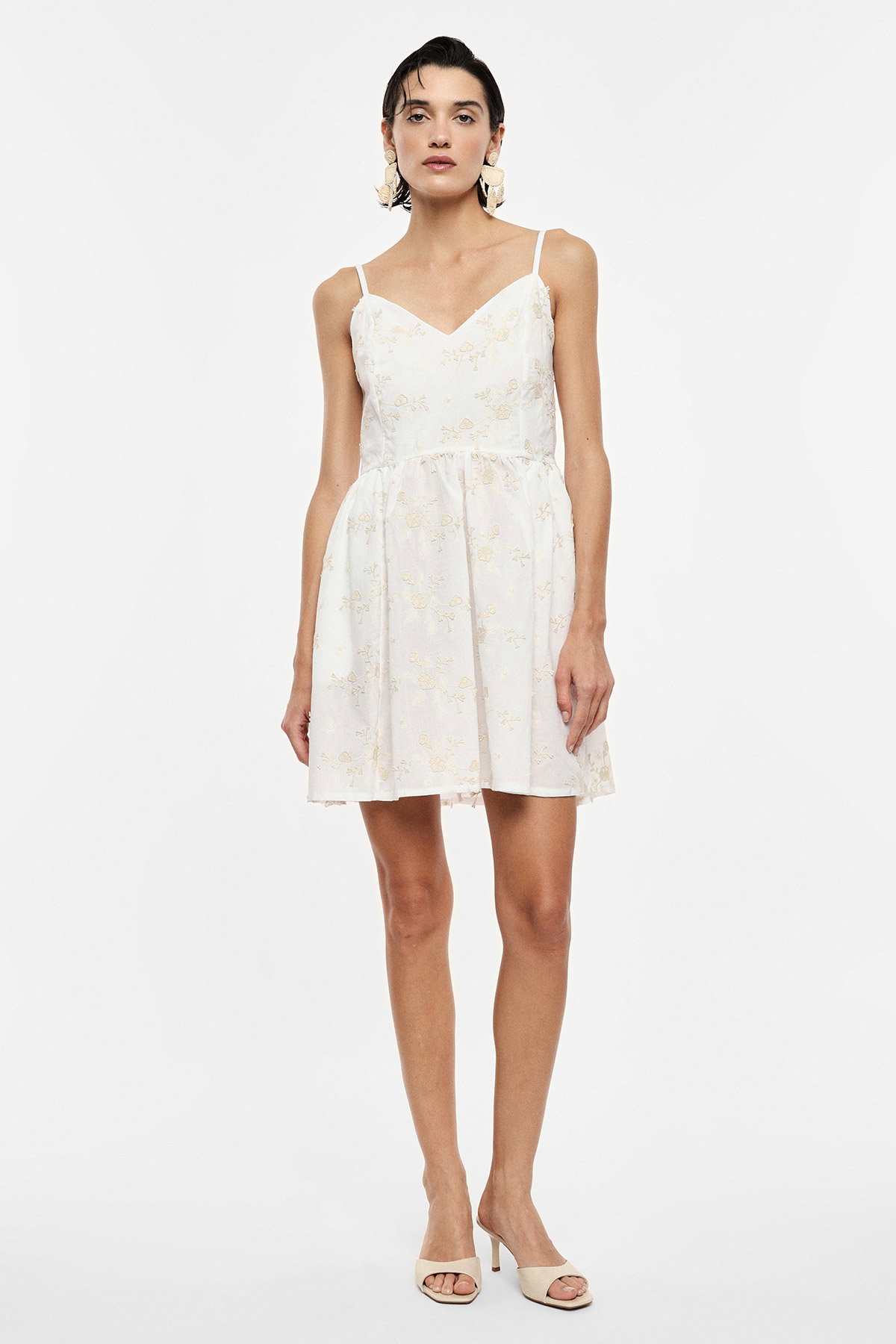 Model in white spaghetti-strap mini dress with gold floral embroidery, V-neck and flared skirt, beige heels