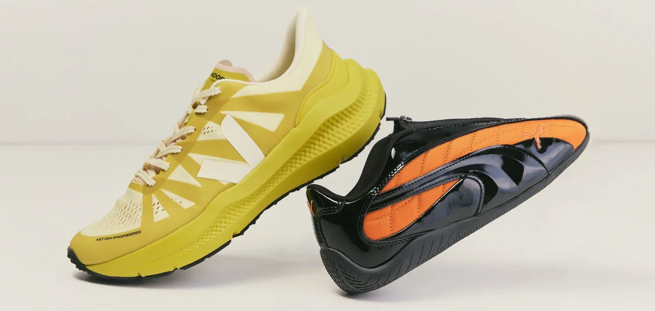 Zapatilla de correr amarilla y zapatilla negra sin cordones con detalles naranjas colocadas una al lado de la otra sobre un fondo liso y claro.