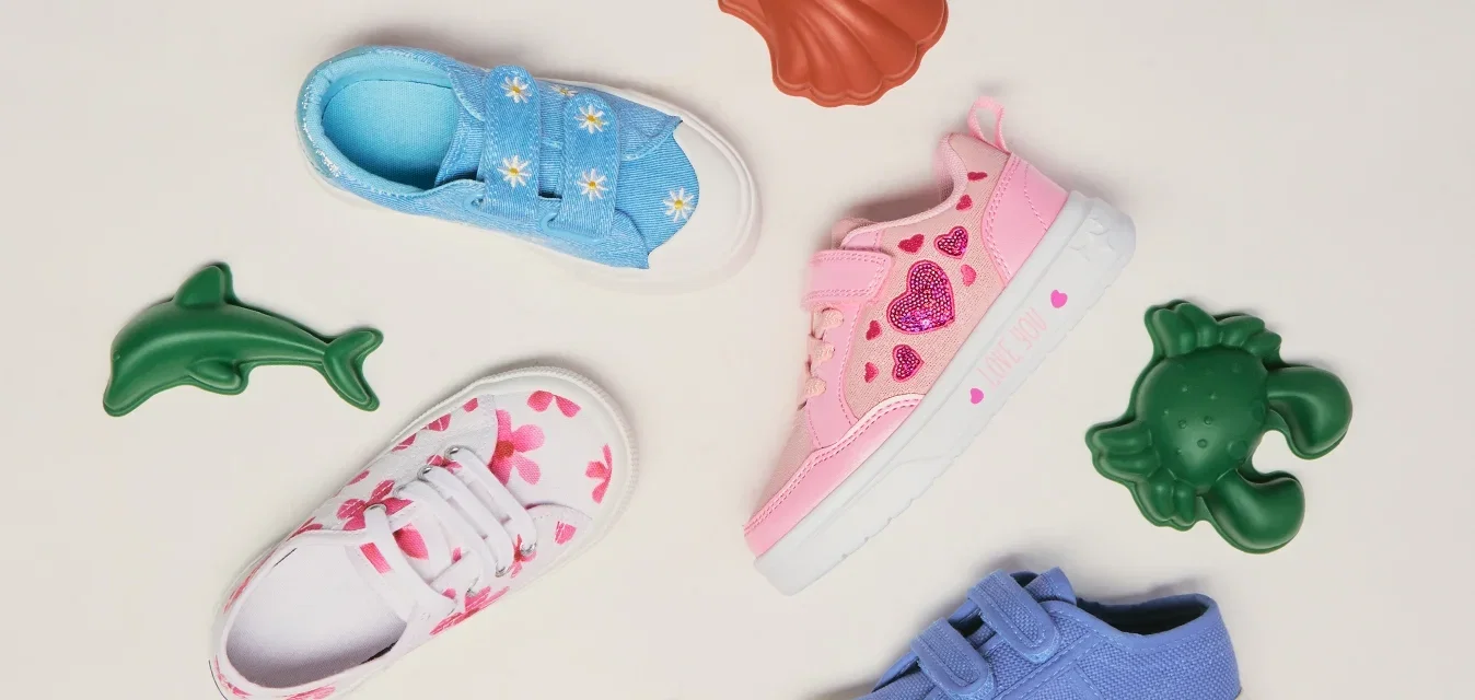 Cuatro zapatillas de bebé coloridas con decoraciones con temática marina rodean juguetes de animales marinos de plástico sobre un fondo liso.