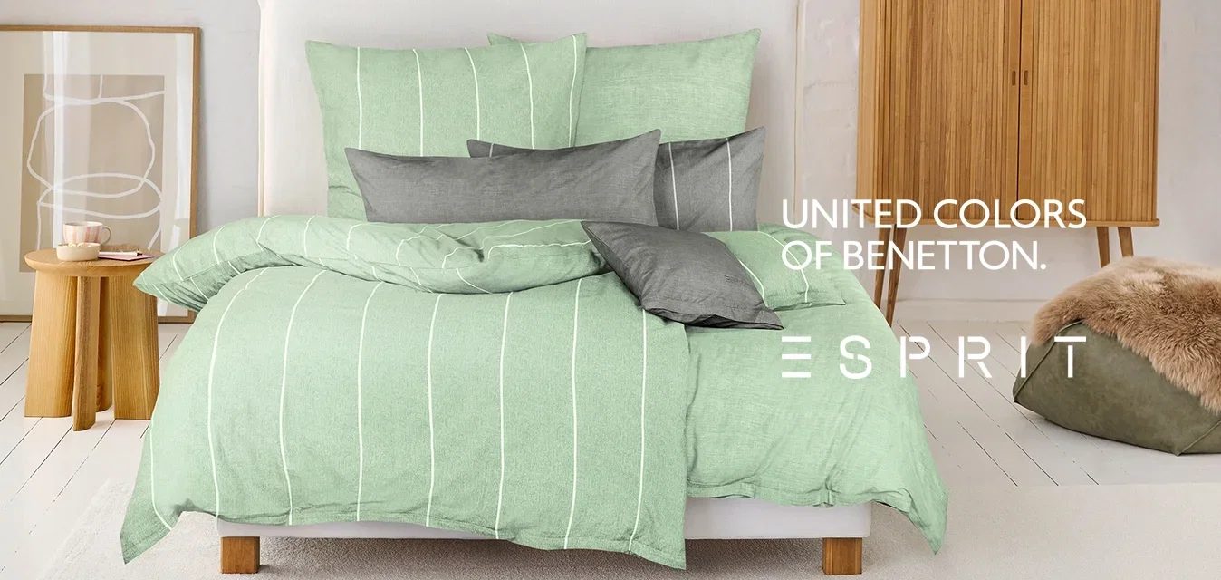 Ensemble de literie à rayures vertes sur un lit avec divers coussins gris. Mobilier en bois clair et un pouf en texture douce dans une chambre minimaliste.