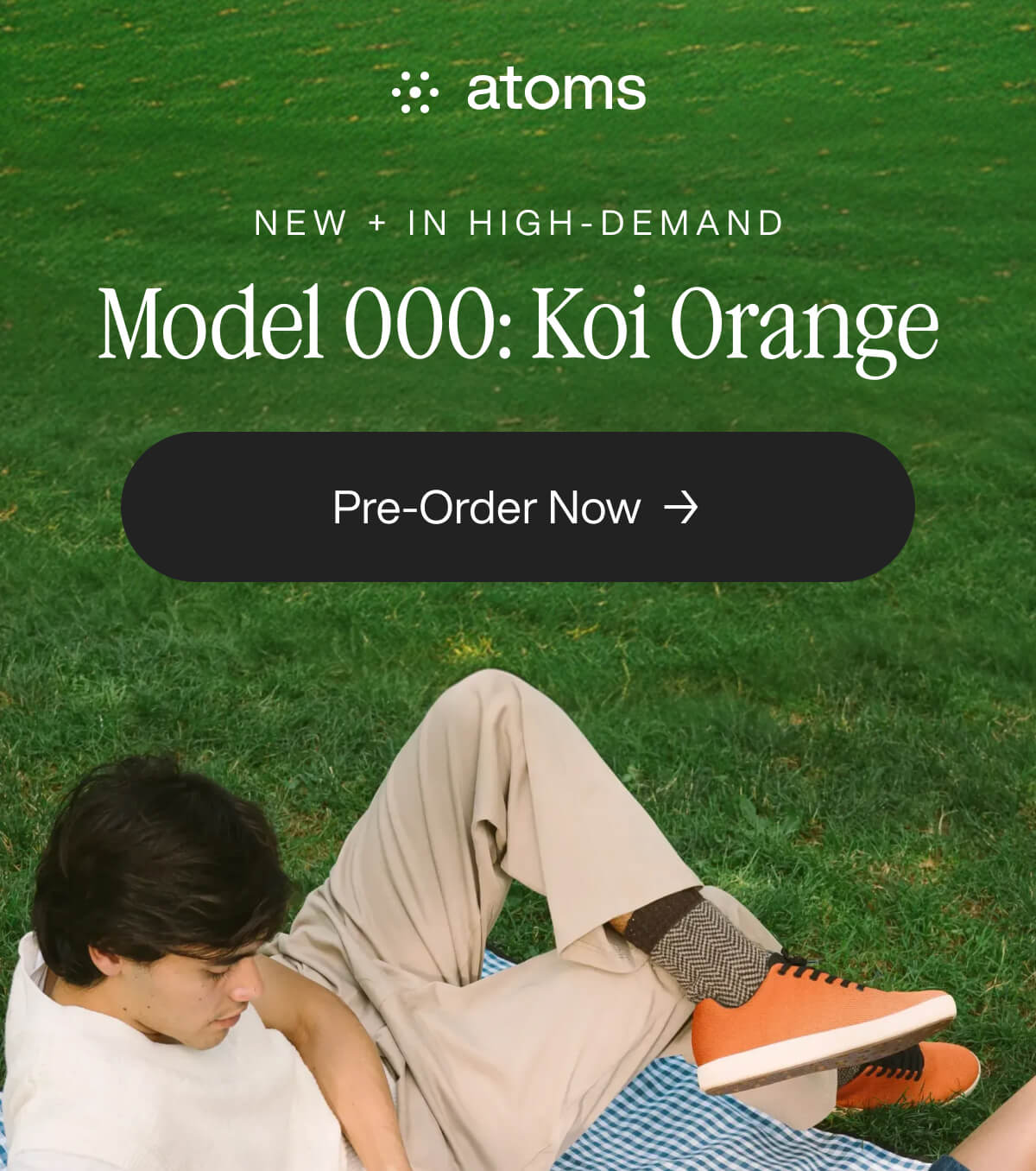 "Man in beige pants and orange sneakers relaxes on grass. Text: "Model 000: Koi Orange" and "Pre-Order Now" on screen."