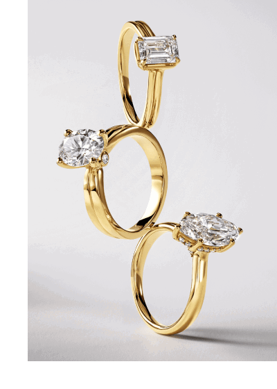 Three stacked yellow gold engagement rings with emerald, oval and marquise-cut diamond center stones.