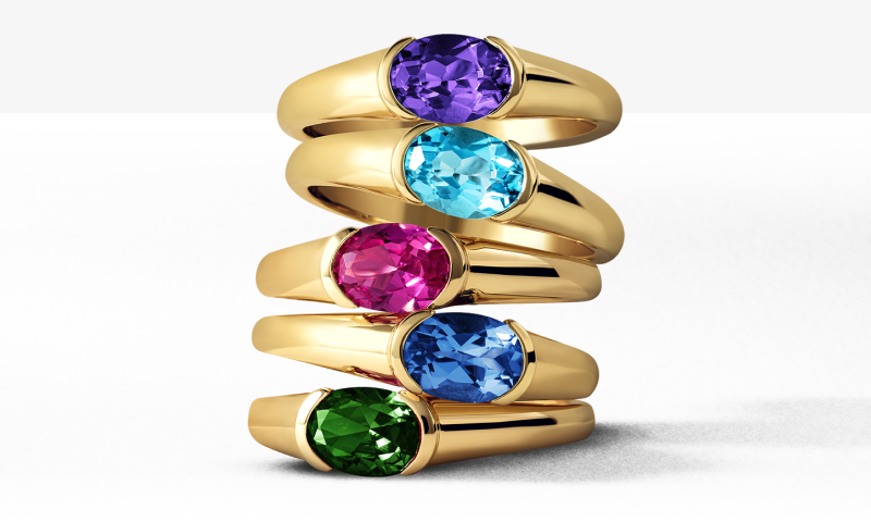 Stack of colorful gemstone rings in yellow gold featuring blue, pink, purple and green stones.