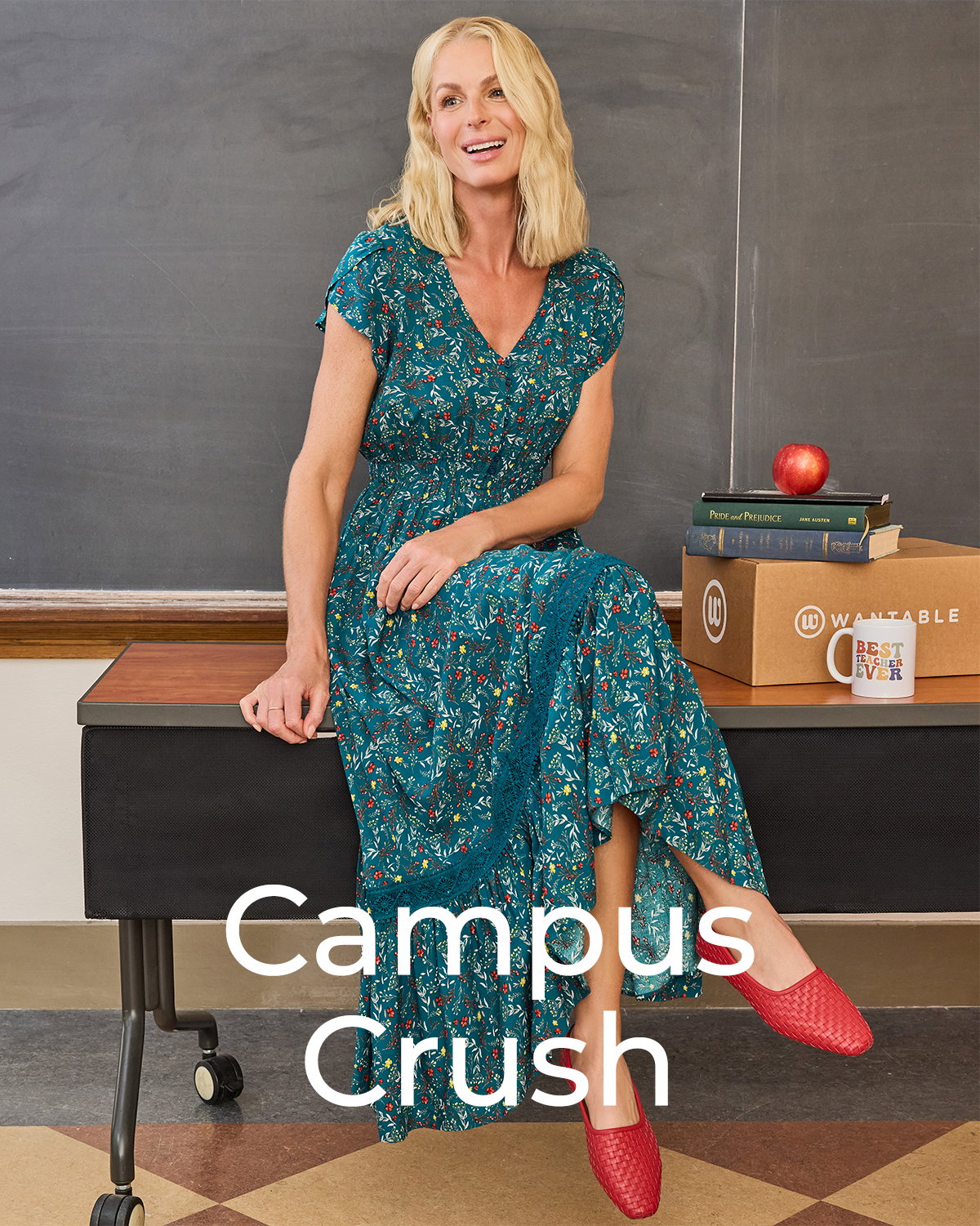 Woman in teal floral dress sits on classroom desk beside books and an apple.