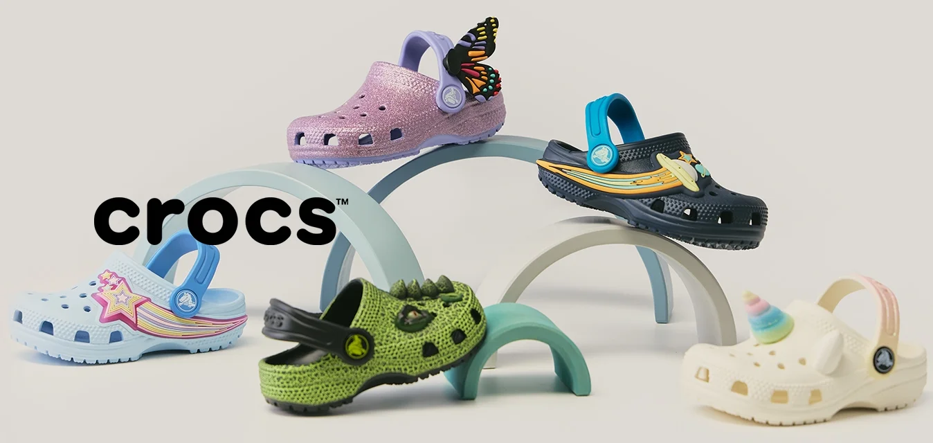 Vijf kleurrijke kindersabots met decoratieve bedeltjes, gerangschikt op pastelkleurige bogen tegen een neutrale achtergrond.