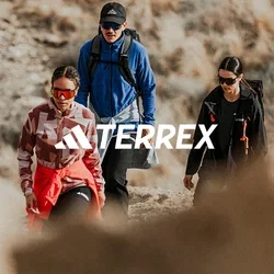 Tres excursionistas con ropa de exterior y gafas de sol caminan por un sendero rocoso en un paisaje seco y cubierto de hierba.