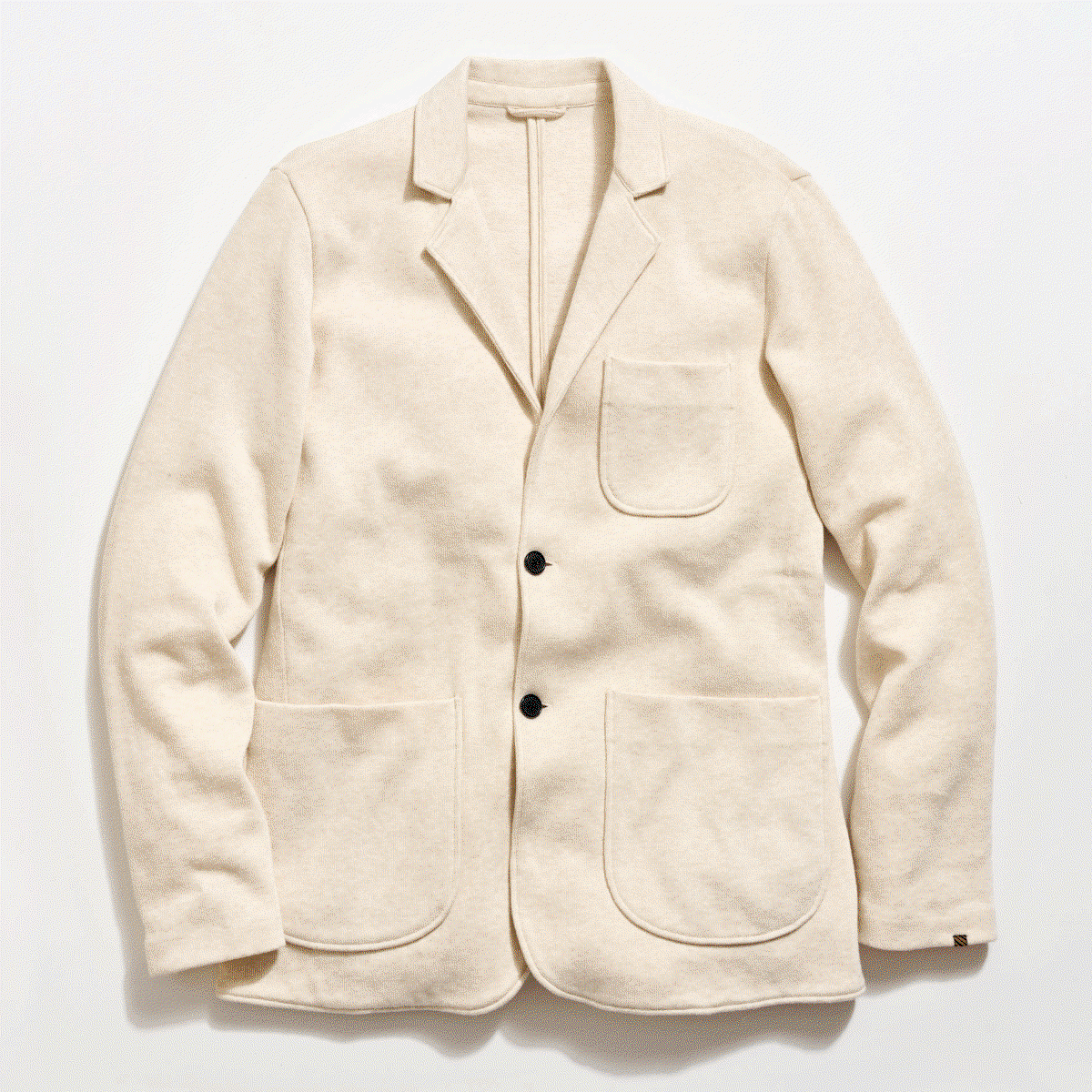 A knit sportcoat in off-white with black horn buttons against a grey background.