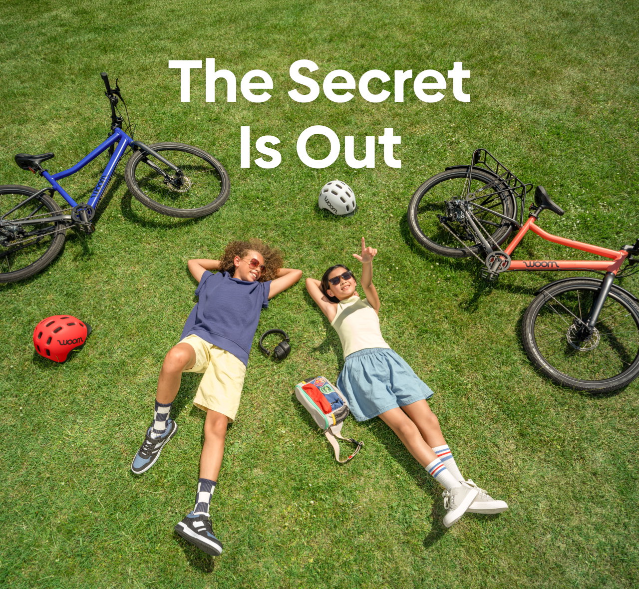Two kids lay on the grass looking at the sky with their woom EXPLORE bikes and READY Helmets laying nearby.