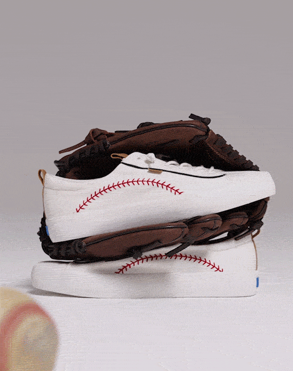 A short video of a baseball rolling toward a pair of Kickback Pennant Washed Twill Slip-On sneakers in white that are sitting with a brown leather baseball glove.