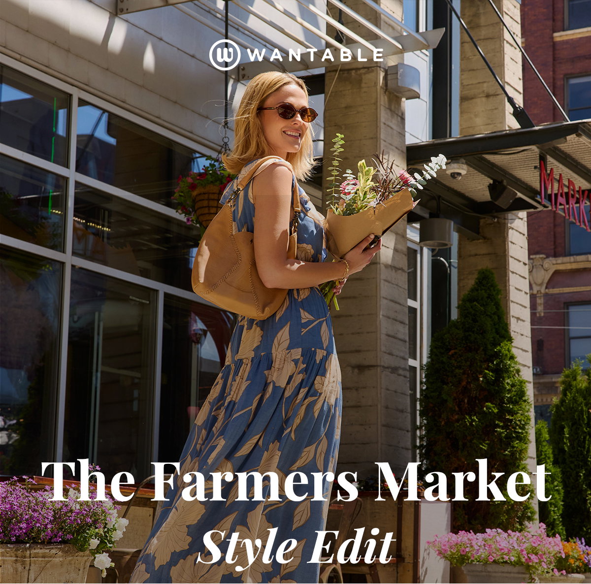 Woman in floral dress carries fresh flowers outside a farmers market on a sunny day.