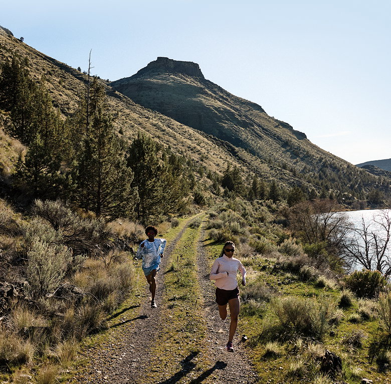 Two people running down a trail by a river.