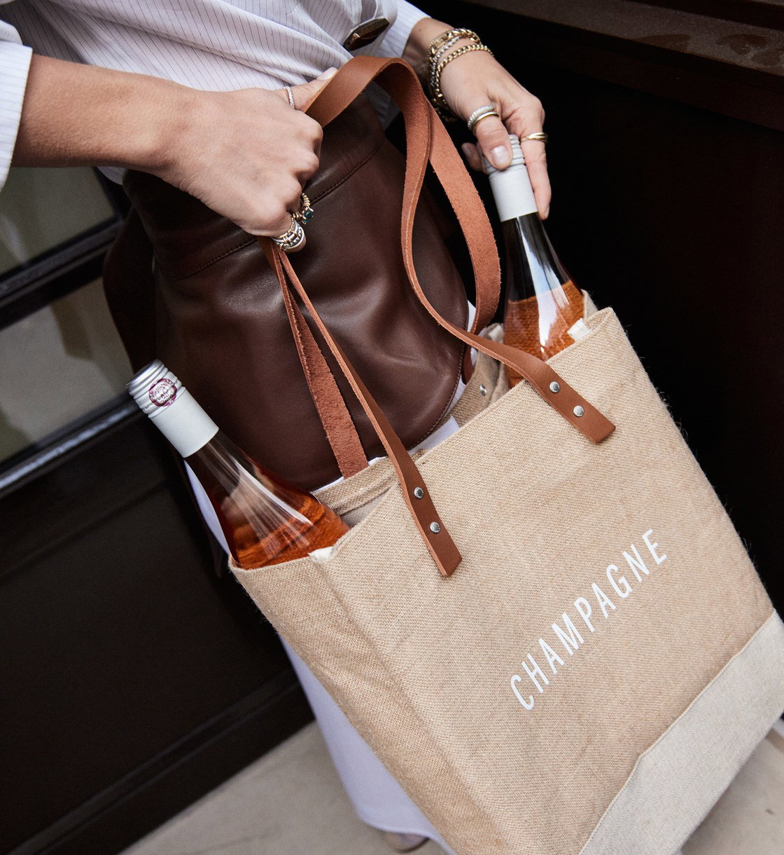 The Apolis Wine Tote in jute, carried with a bottle of champagne