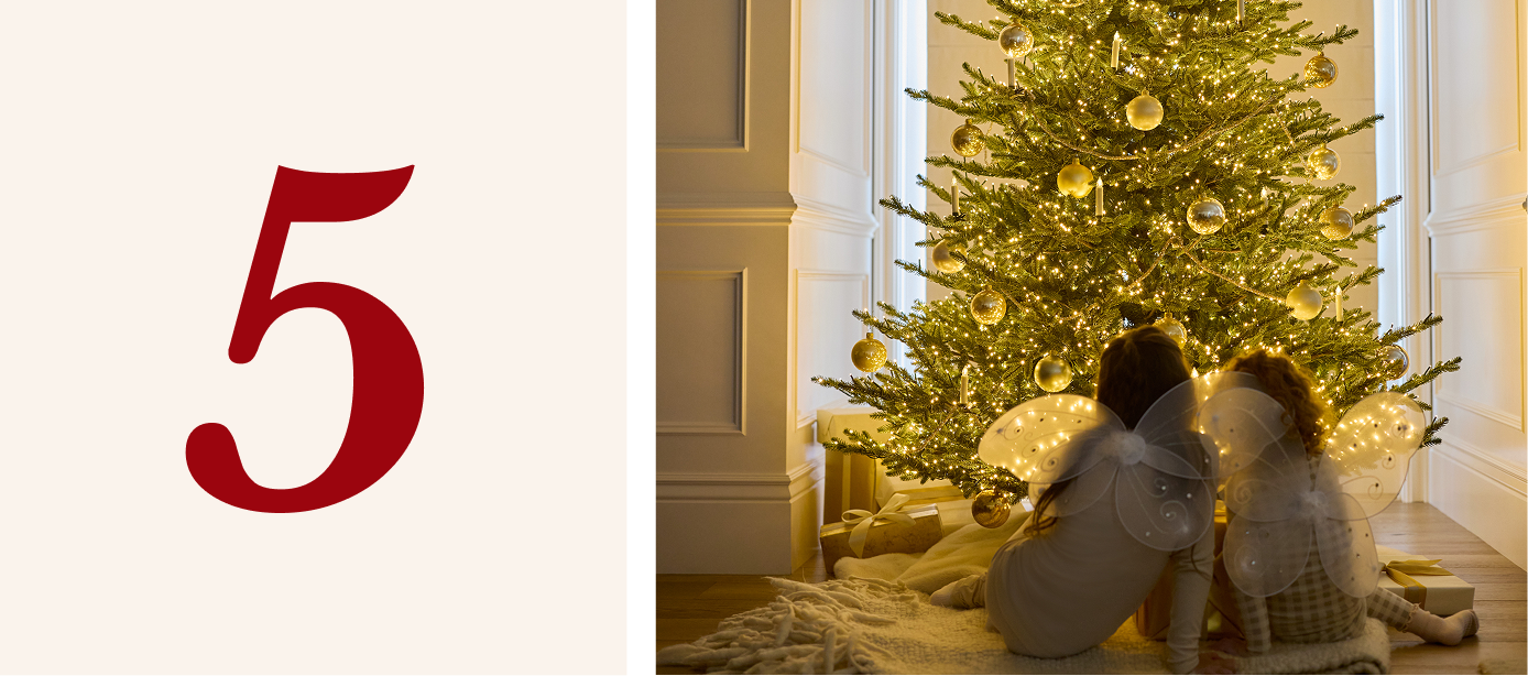 Two girls sitting in front of a pre-lit Christmas tree