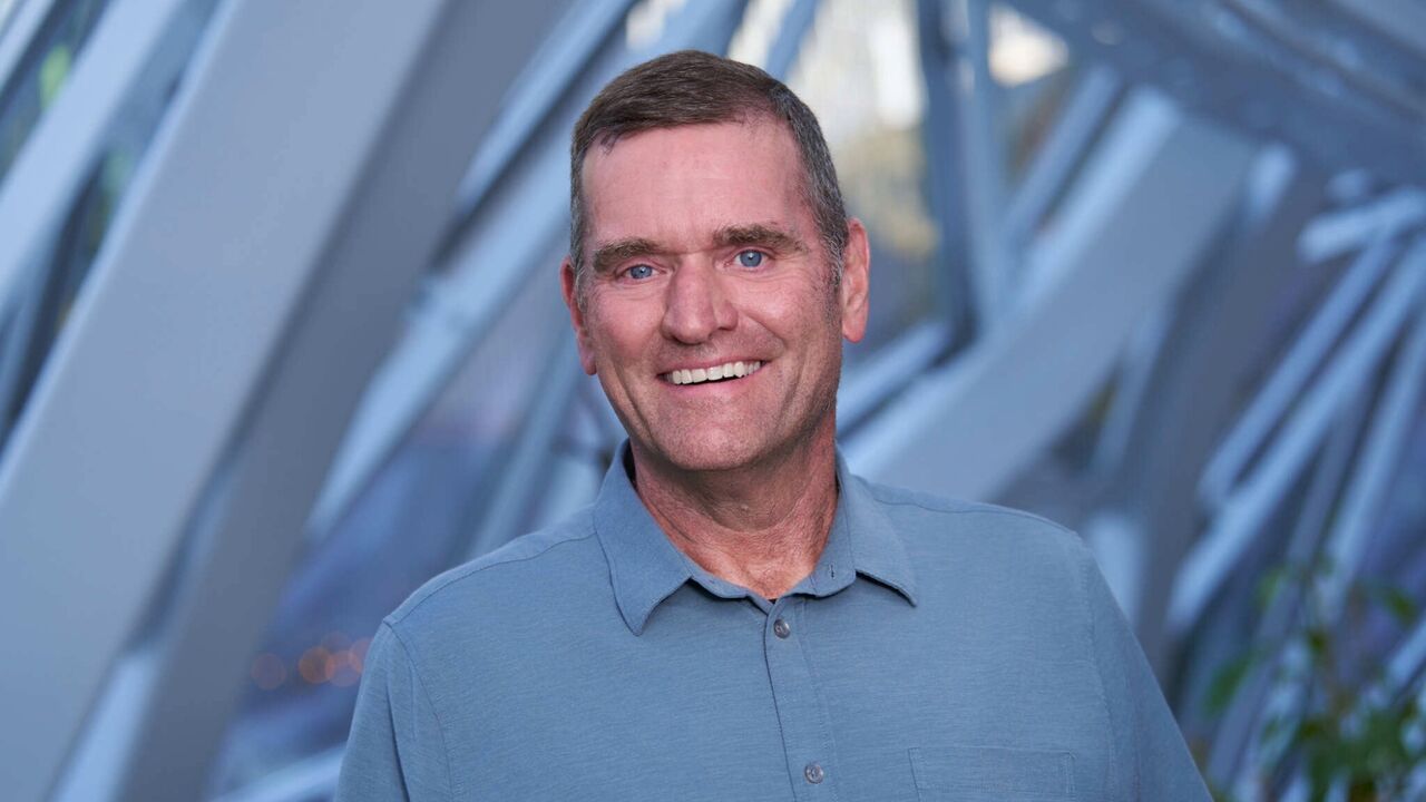 Professional headshot of a smiling man wearing a slate-blue polo