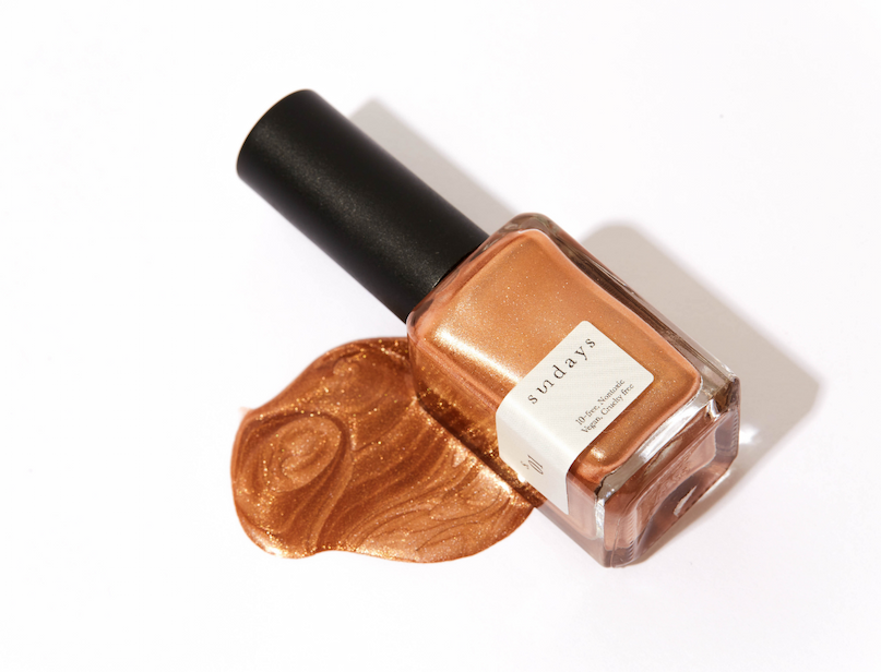 Copper shimmer nail polish bottle with a swatch of matching polish on a white background.