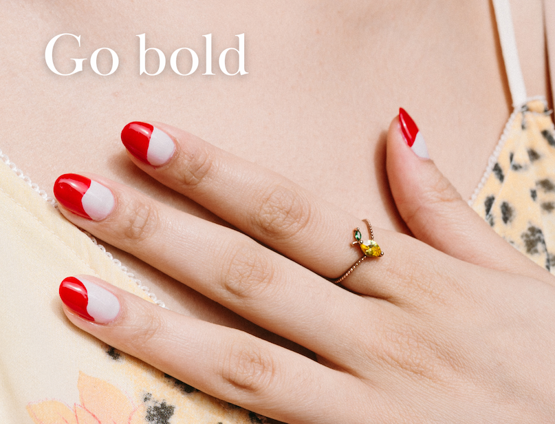 Hand with red and white nail art wearing a gold ring. Text reads, "Go bold."