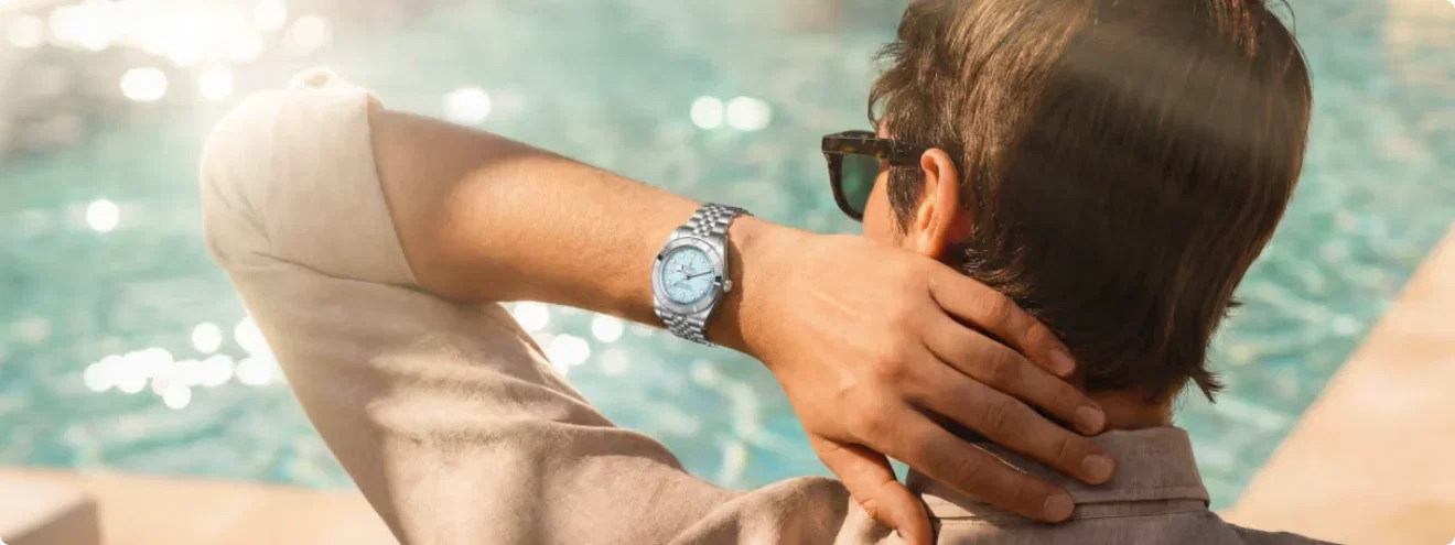 Man wearing a TUDOR blue dial luxury watch by a swimming pool in summer