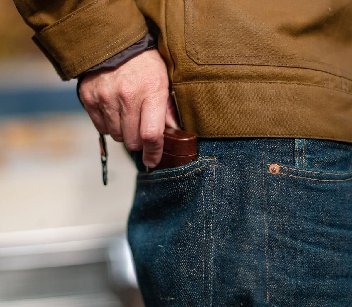 A man slides a brown leather AirPods case into the front pocket of his jeans.