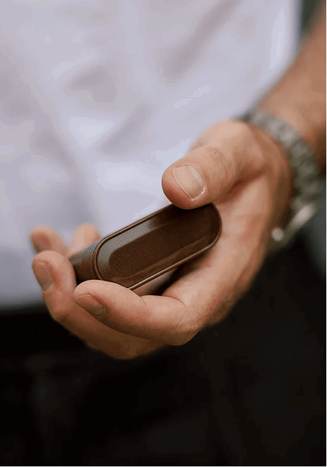 A hand holding a small dark brown leather AirPods case with rounded edges.