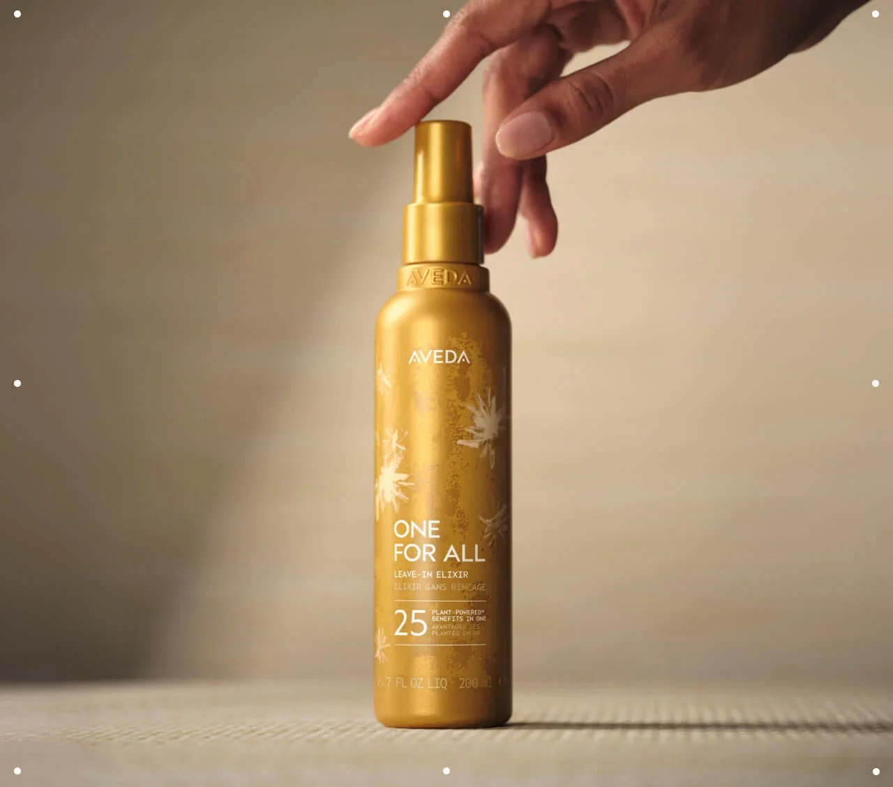 Close-up of a hand reaching out for a bottle of Aveda One For All Leave-In Elixir.