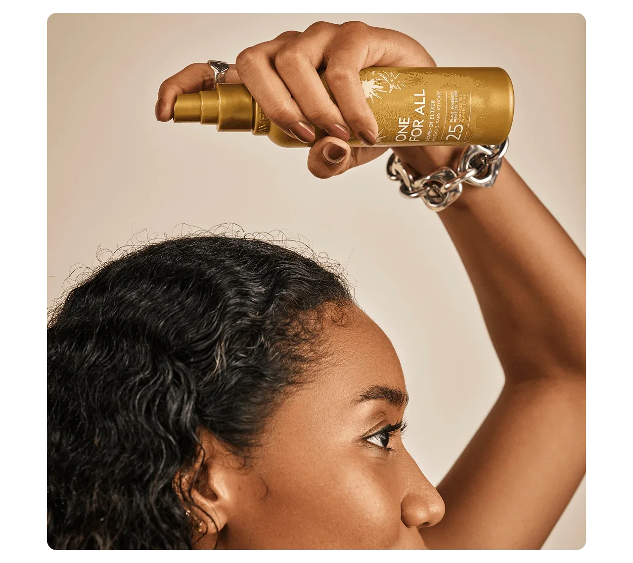 Close-up of a woman applying Aveda One For All Leave-In Elixir to her hair.