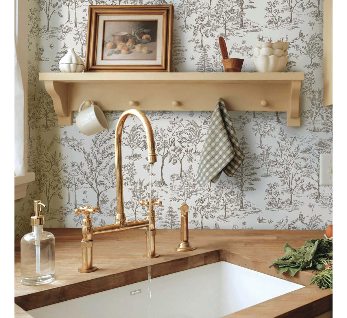 Image of Tempaper's Arbor Toile wallpaper in cocoa installed in a kitchen behind a sink. A shelf with knicknacks and a picture is seen on the wall. 