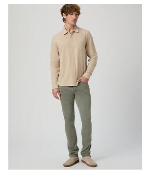 Image of a man wearing a beige button up and sage green denim jeans.