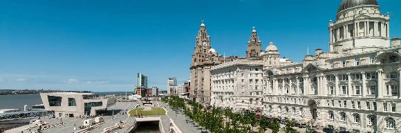 A panoramic view of Liverpool's waterfront featuring historic buildings and a clear blue sky.
