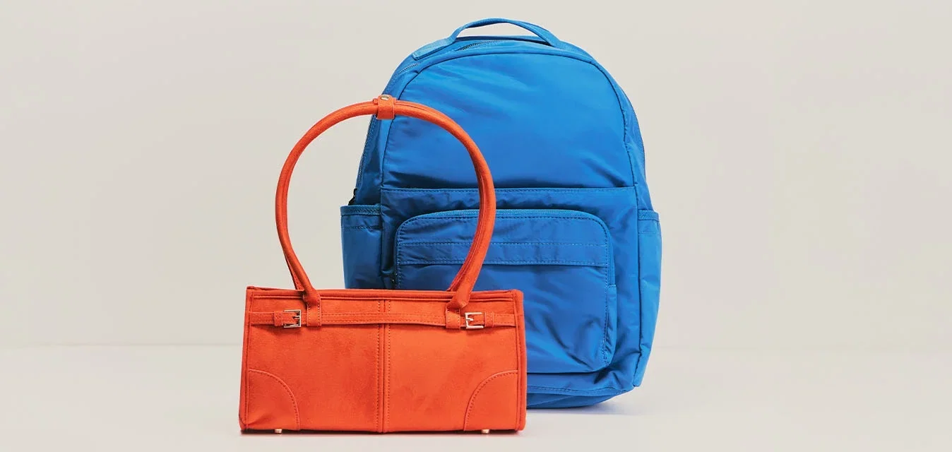 Zaino blu posizionato dietro a una piccola borsa arancione con due manici su sfondo beige chiaro.