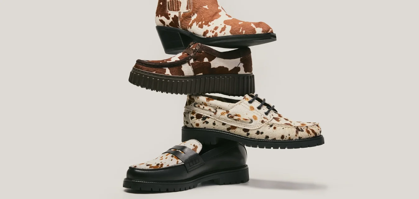 Pila de cuatro zapatos con varios diseños, incluyendo estampado de vaca marrón y blanca, estampado de leopardo y color marrón oscuro sólido, sobre un fondo claro.