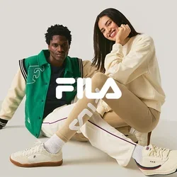 Dos personas sentadas en el suelo, una con una chaqueta varsity verde y blanca, la otra con mallas beige y un suéter crema, sonriendo.