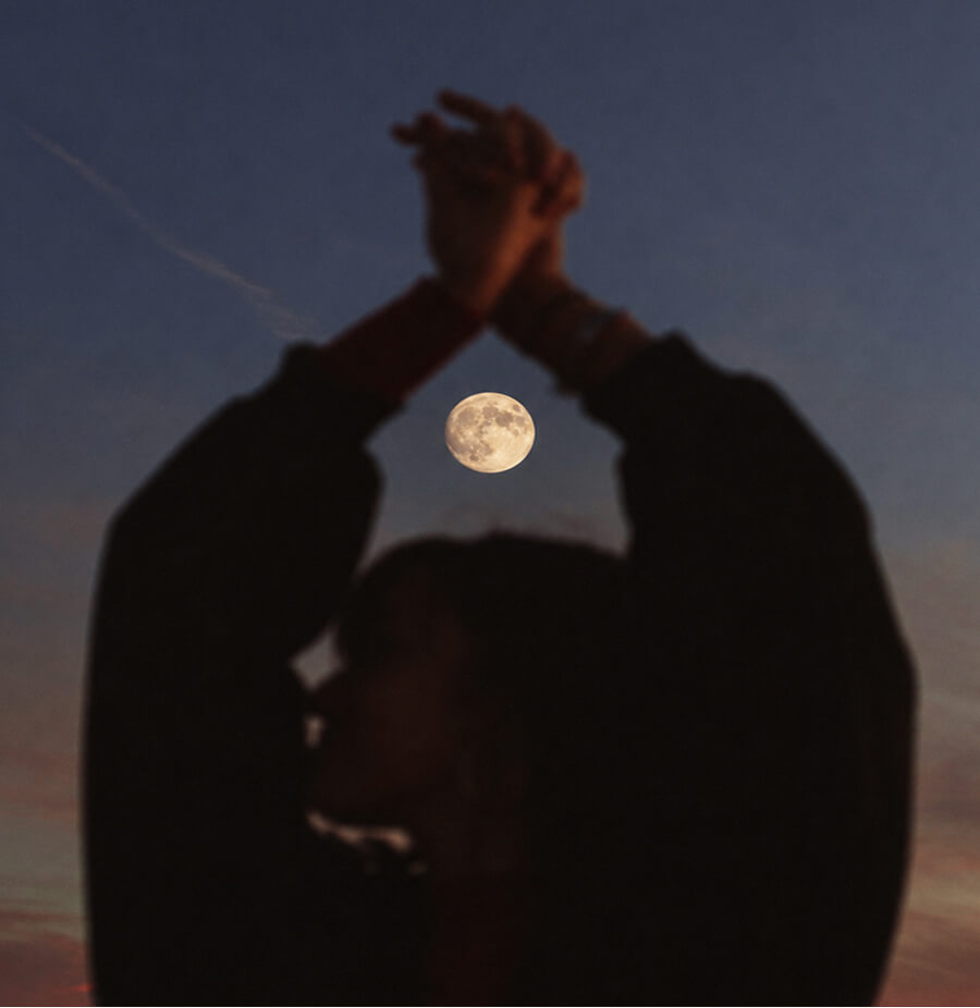 Silhouette of a woman stretching in front of a full moon.