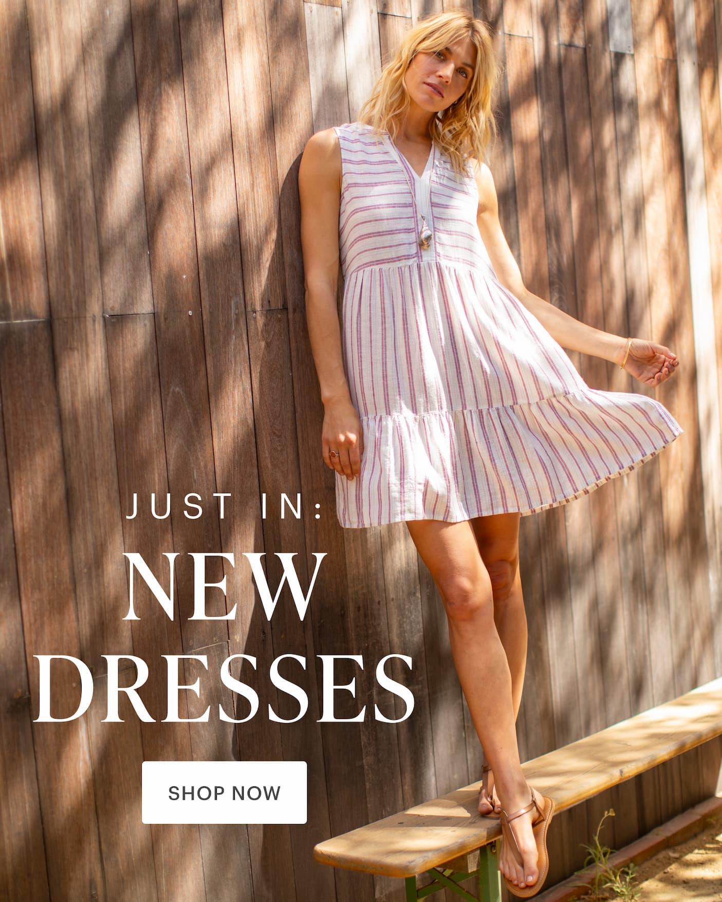 Just In: New Dresses - Shop Now. Woman in red and white striped Nellie Dress in front of wood wall. 