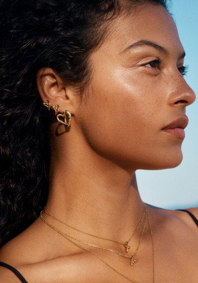 A model stares ahead in 14k gold-plated heart-shaped Pandora earrings.