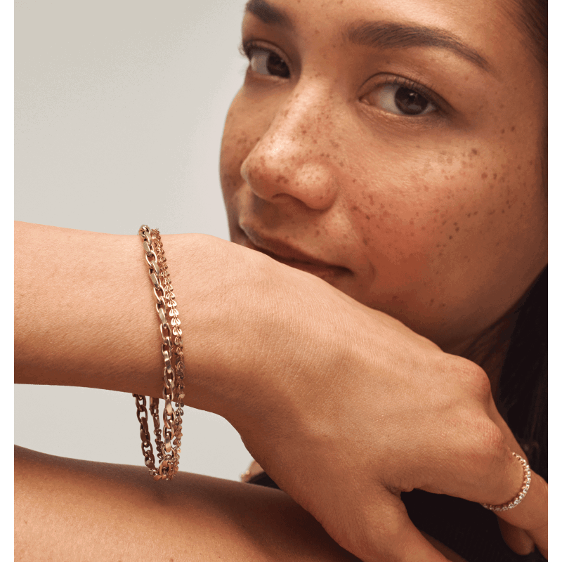 Woman wearing layered yellow gold chain bracelets and a diamond band ring.