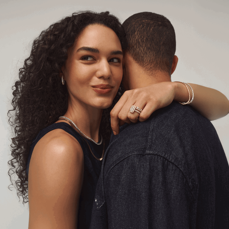 Woman embracing her partner while wearing hoops, necklaces, a diamond tennis bracelet and a ring. 