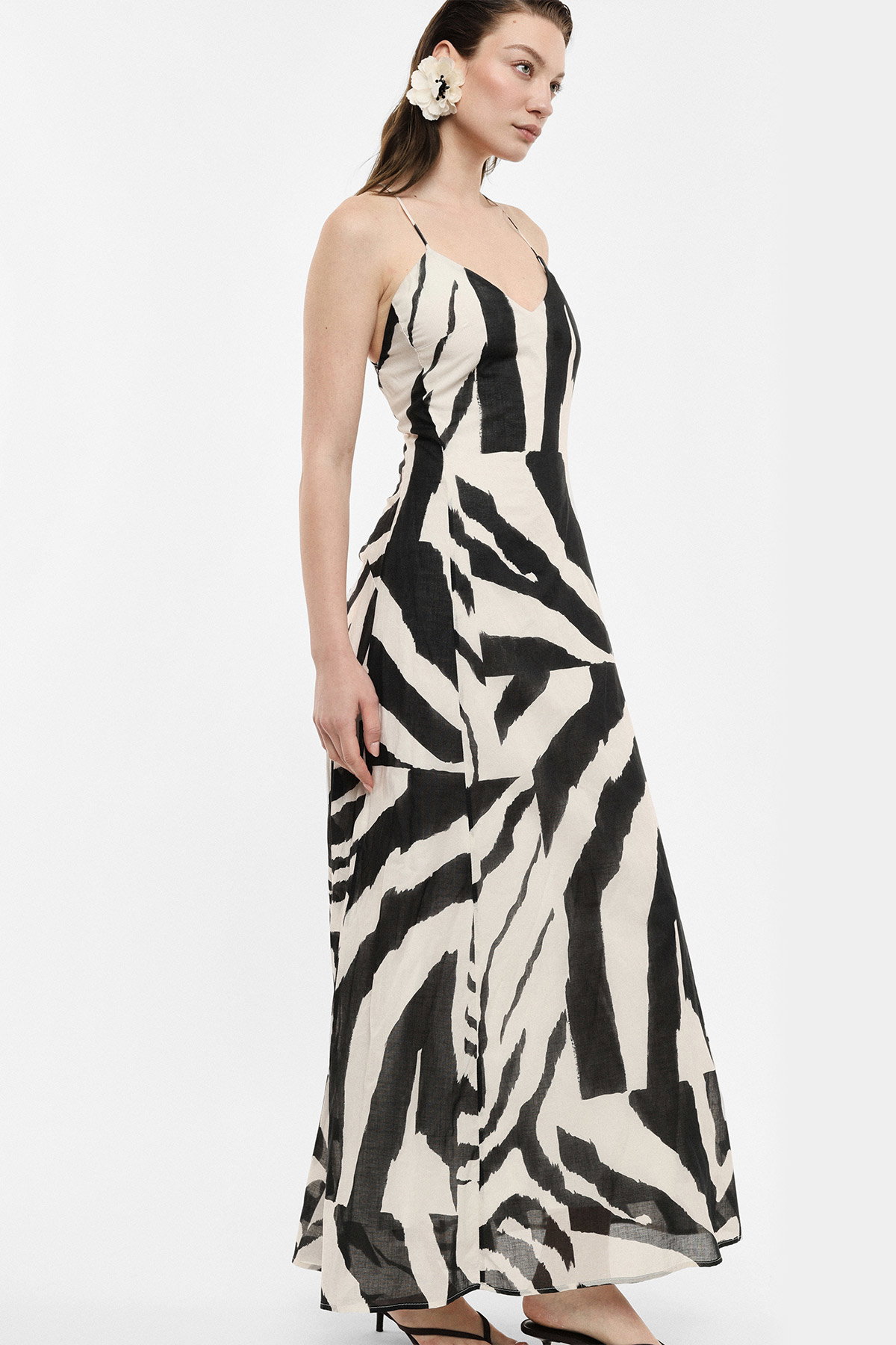 Side-view of a woman wearing a black-and-white zebra-print maxi dress with thin straps and a white flower earring, studio shot