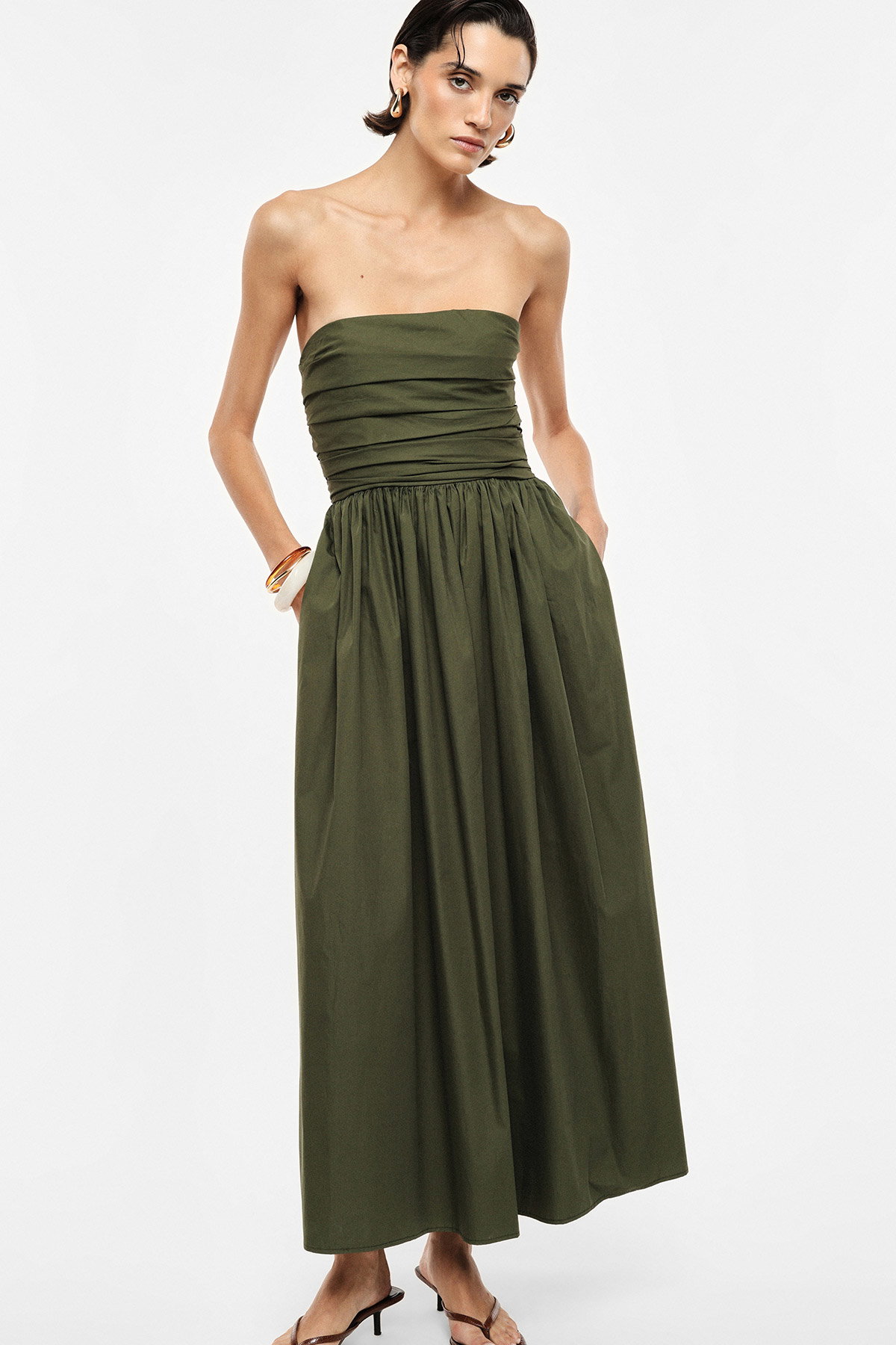 Model in strapless olive-green maxi dress with ruched bodice, side pockets and sandals