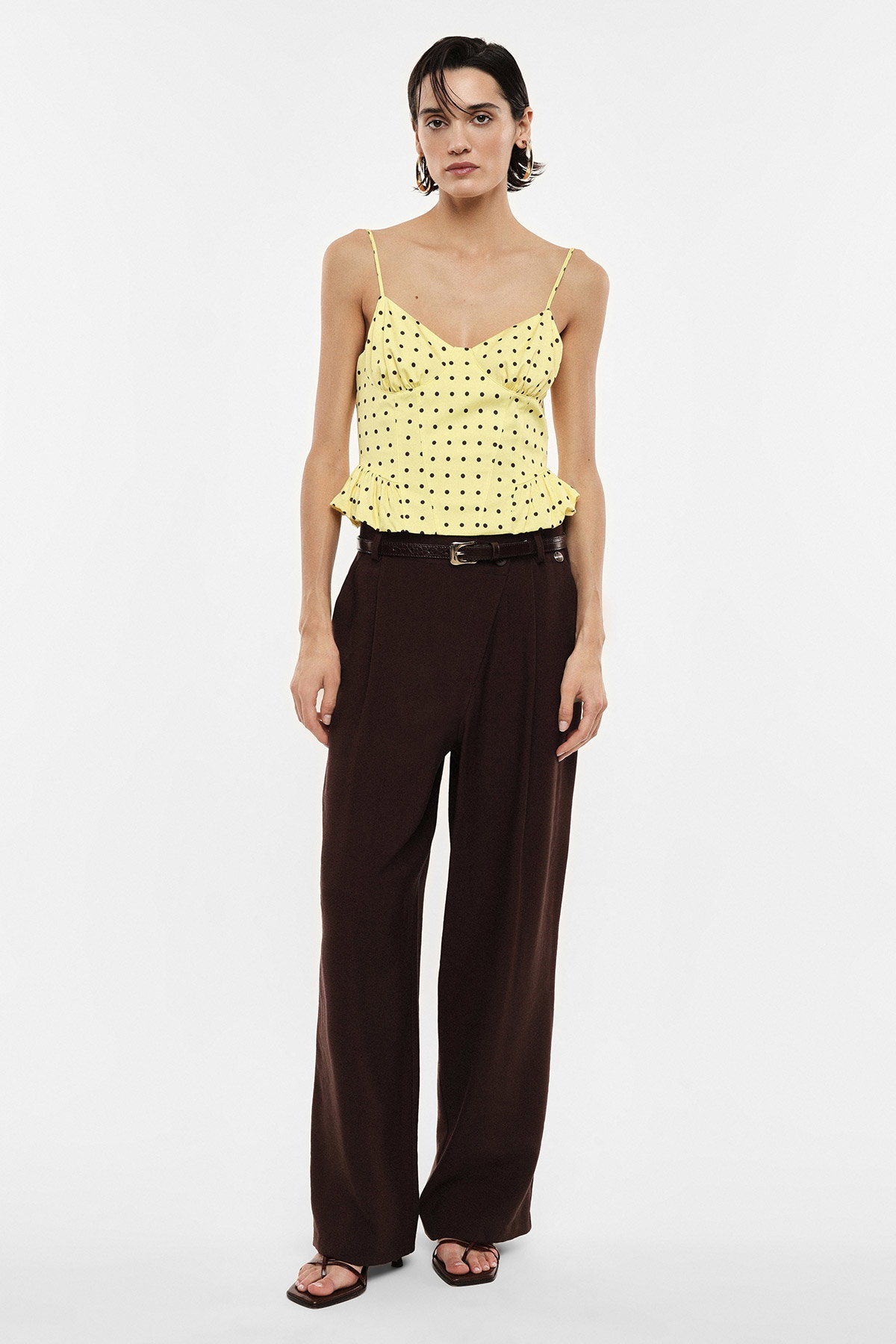 Full-length shot of woman modelling yellow polka-dot ruffled camisole and wide-leg brown trousers on white background