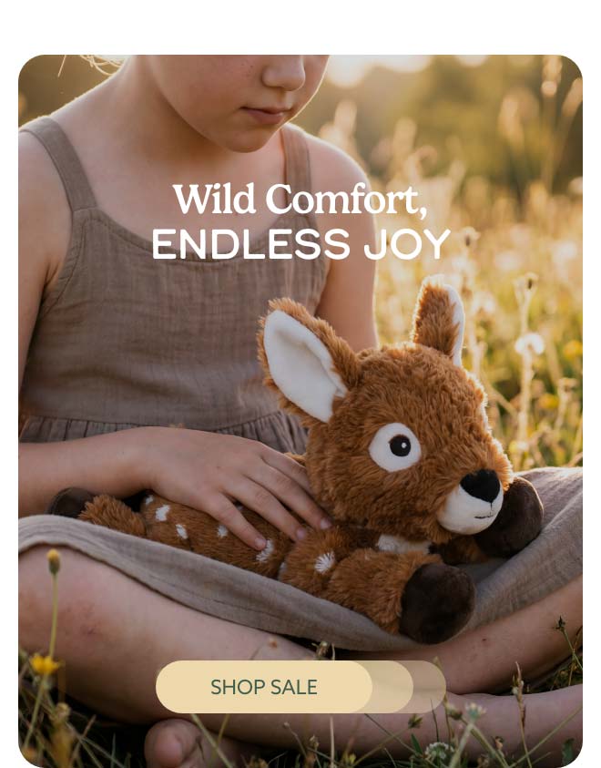 A child in a field with Deer Warmies resting in their lap. Shop Sale.