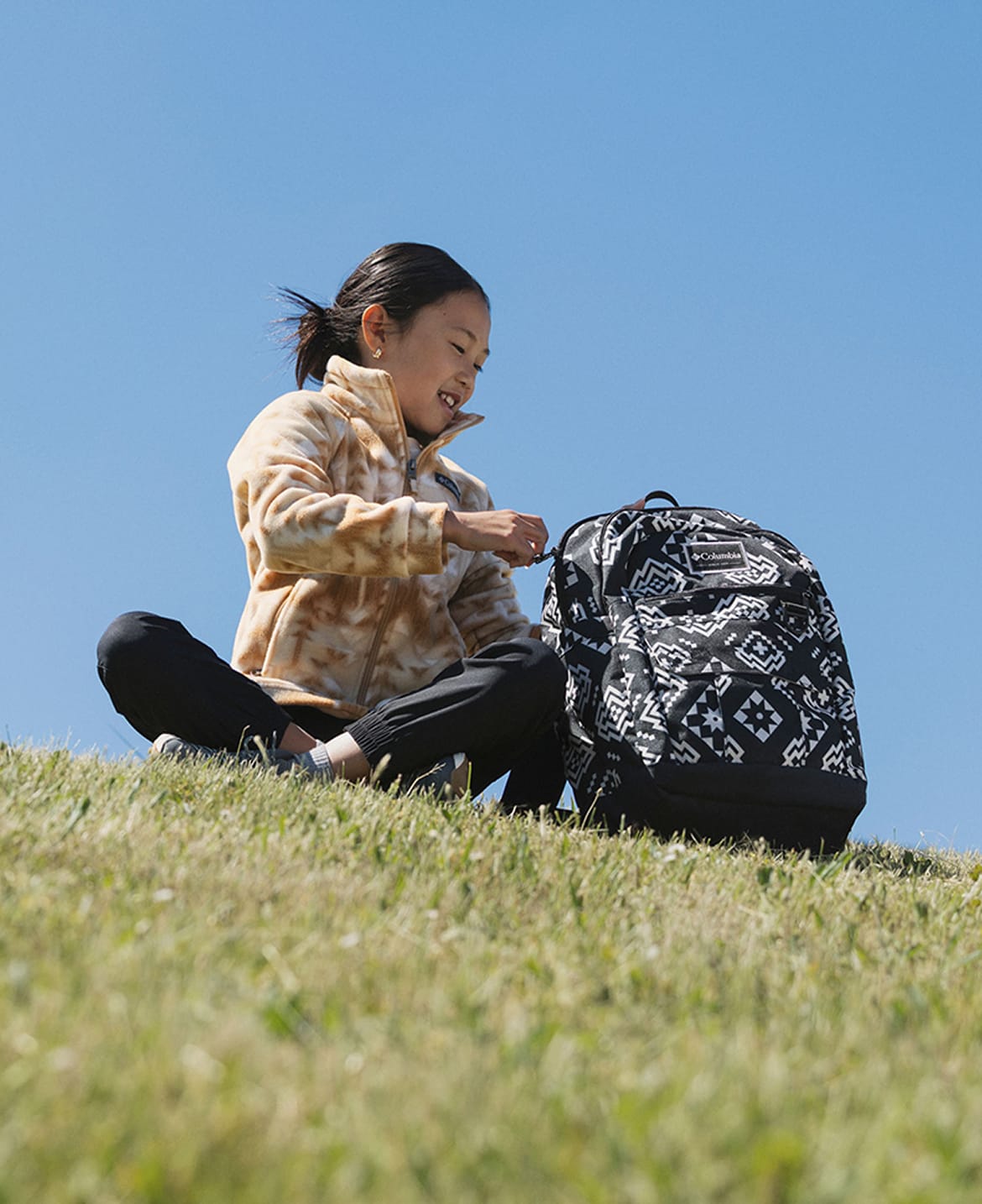 A girl sitting in the grass with a backpack next to her