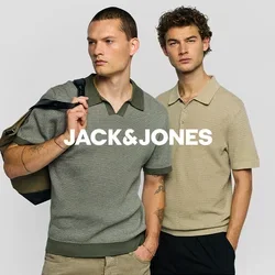 Due uomini stanno fianco a fianco indossando polo in maglia a maniche corte, uno grigio con colletto verde e borsa a tracolla, l’altro beige con le mani in tasca.