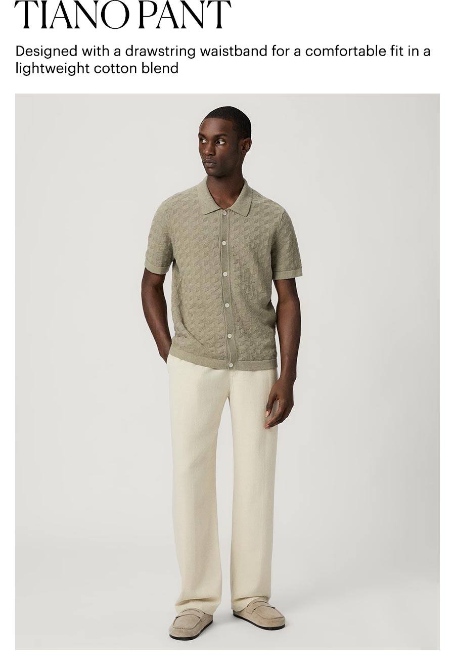 Tiano Pant - Designed with a drawstring waistband for a comfortable fit in a lightweight cotton blend. Featuring a man wearing a pair of cream cotton loose-fit pants with a sage knit short sleeve button-up with suede slippers.