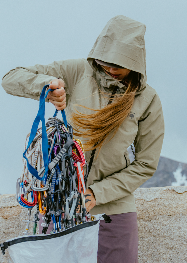 A climber pulling out her gear while wearing the Women's Chockstone™ Alpine LT Hooded Jacket.