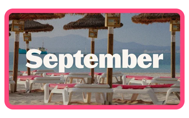 Beach scene with rows of white sun loungers topped with bright pink cushions beneath thatched parasols. Calm blue sea and hazy mountains are visible in the background, with a boat offshore. Large white text reading 'September' is centered across the image, which is enclosed by a bright pink border.