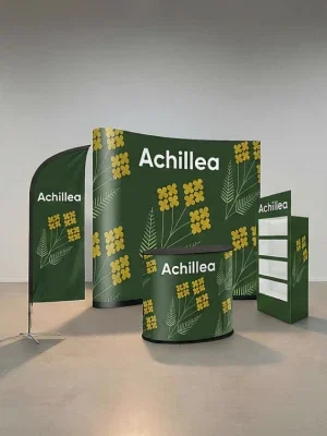 Stand fieristico con sfondo verde, motivi floreali gialli e la scritta “Achillea” su diversi elementi